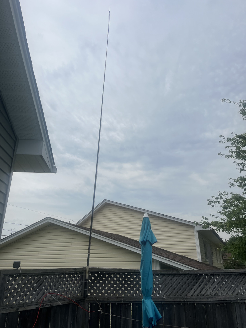 View of a fence between two houses with a 5-metre-tall vertical antenna affixed to it.